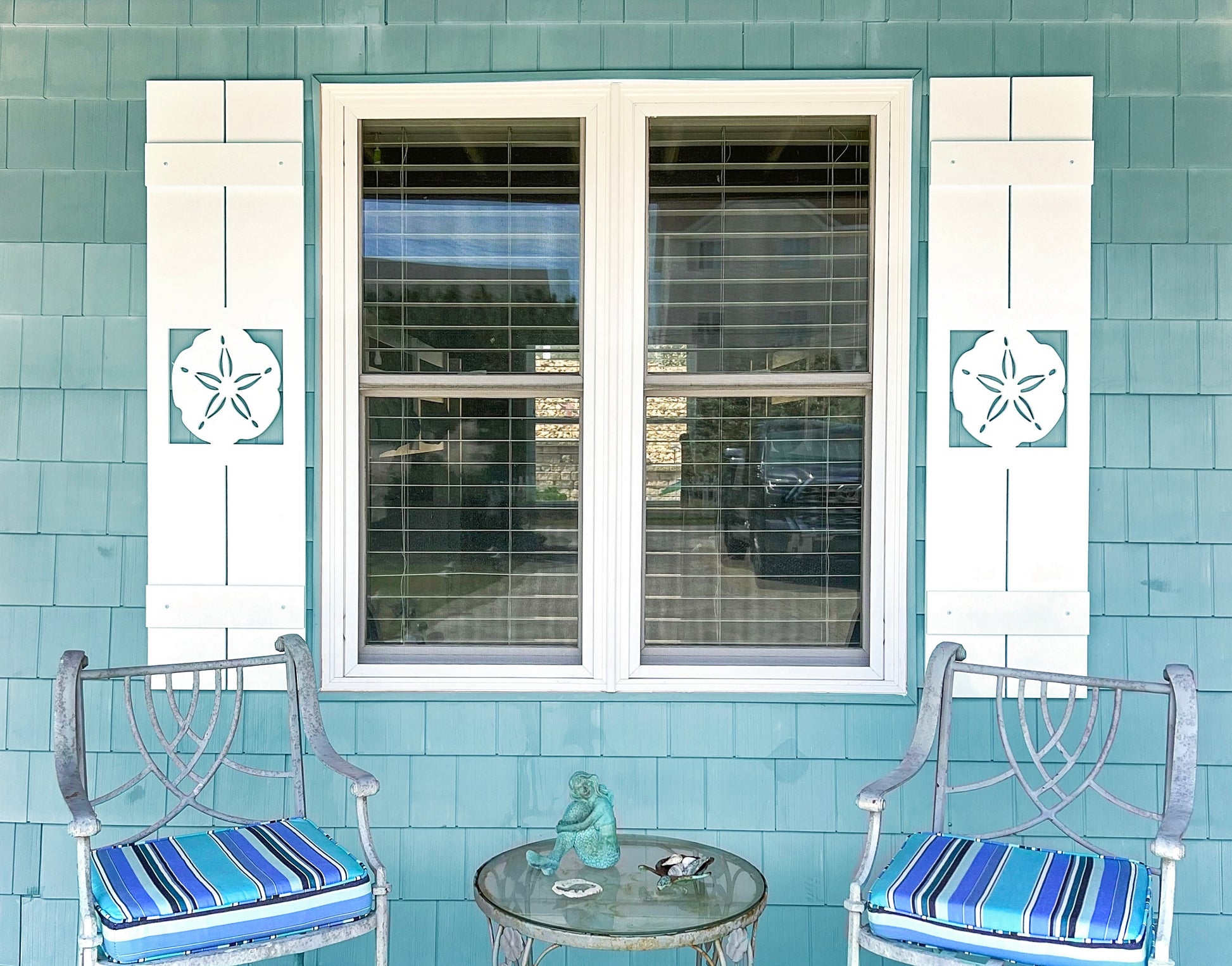 Exterior board and batten style coastal window shutters with sand dollar cutout. Weatherproof PVC beach house shutters for outdoor decor.